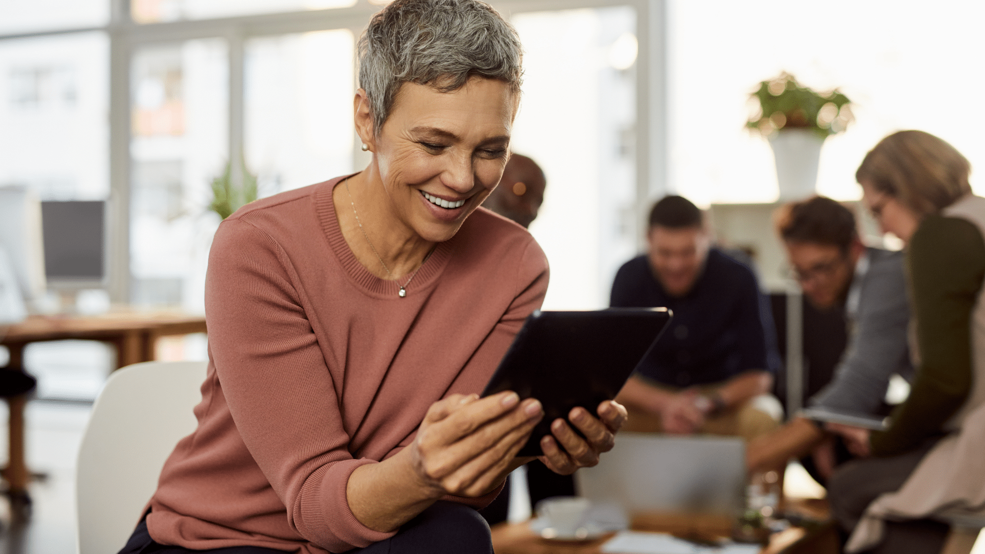 Une femme qui sourit en regardant une tablette qu'elle tient dans ses mains